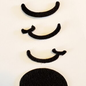 May include: Four black felt shapes, three are curved and one is a circle. The curved shapes are arranged vertically, with the largest at the top and the smallest at the bottom. The circle is below the three curved shapes.