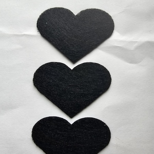 May include: Three black felt hearts stacked on top of each other on a white background.
