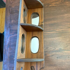 May include: A wooden corner shelf with a dark brown finish. It features two shelves and three oval openings. The shelf is designed to fit into a corner and has a decorative bottom edge. The wood grain is visible.