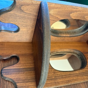 May include: A wooden wine rack with a dark brown finish. The rack has two levels with oval openings for bottles. The sides have decorative, curved cutouts. The wood grain is visible.