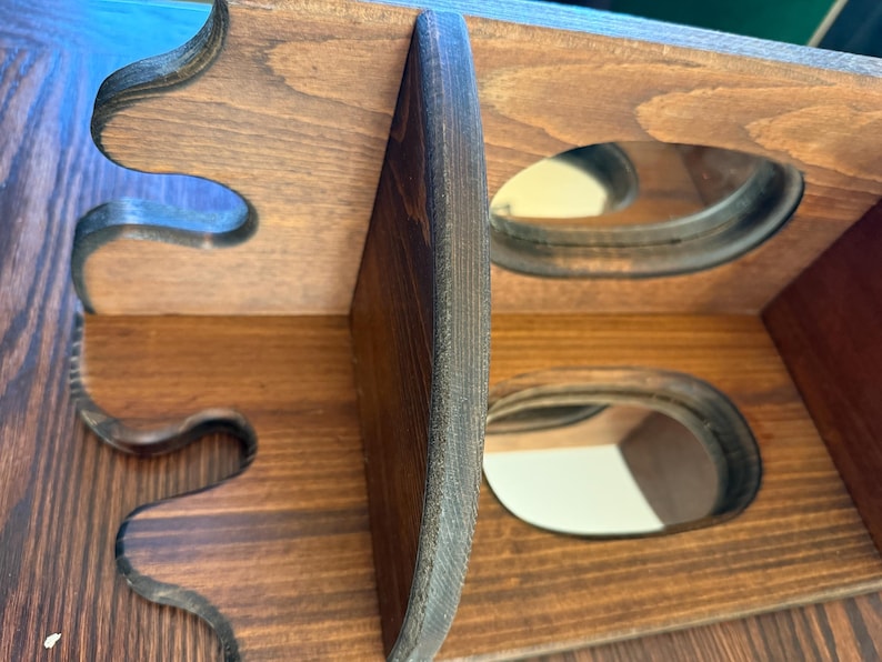 May include: A wooden wine rack with a dark brown finish. The rack has two levels with oval openings for bottles. The sides have decorative, curved cutouts. The wood grain is visible.