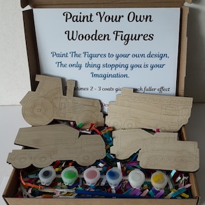 May include: A wooden craft kit containing five unfinished wooden figures of a tractor, dumper truck, fire engine, excavator, and bulldozer. The kit includes six small pots of paint and two paintbrushes. The box has a white card insert with the text "Paint Your Own Wooden Figures" and instructions to paint the figures to your own design.