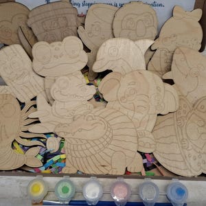 May include: A collection of unfinished wooden cutouts in various animal shapes, including a frog, elephant, and shark. The set includes small paint pots with yellow, green, white, pink, and blue paint, along with paintbrushes. The cutouts are in a cardboard box.