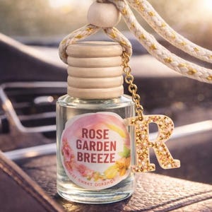Può includere: Flacone di profumo per auto in vetro trasparente con tappo in legno ed etichetta "Rose Garden Breeze". È appeso a una corda bianca e dorata con una catena dorata e un ciondolo a forma di lettera "R" dorata glitterata.