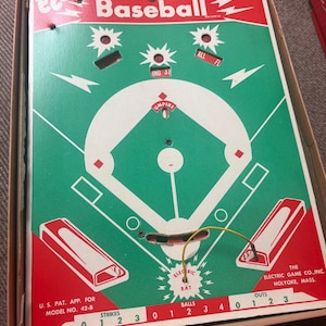 May include: Vintage Electric Baseball game in its original box. The game board features a green baseball field design with red accents and text. Includes a bat, strike and out counters, and the text "Electric Baseball".