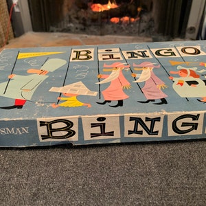 May include: Vintage blue and white cardboard game box with the word "Bingo" printed in large black letters. The box features a colorful illustration of cartoon characters in a parade.