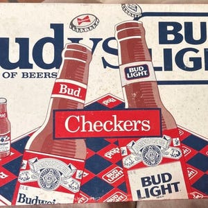 May include: A vintage Budweiser and Bud Light beer box with a checkerboard design. The box features large illustrations of beer bottles and the text "Bud Light" and "King of Beers". The overall color scheme is red, white, and blue.