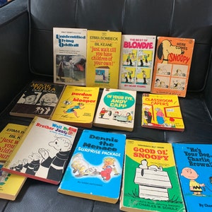 May include: A collection of vintage paperback books featuring popular comic strips, including Peanuts, Blondie, Dennis the Menace, and Andy Capp. The books are in various colors, including yellow, blue, red, and green. The covers feature illustrations of the characters from the comic strips.
