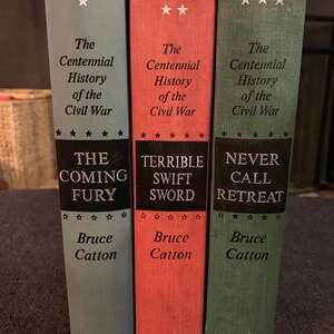 May include: Three hardcover books with blue, red, and green covers. The books are part of a series called "The Centennial History of the Civil War" by Bruce Catton. The titles are "The Coming Fury", "Terrible Swift Sword", and "Never Call Retreat".