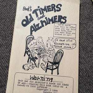 May include: A tan-colored book cover titled Book 6 Old Timers and Alzhimers. The cover features a black ink illustration of two people playing a board game, with speech bubbles containing text. A warning box at the bottom includes text and the date 1990.