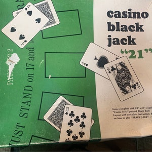 May include: A green and white game box for a casino-style black jack game. The box has the text "BLACK JACK" on the front, along with the text "casino black jack "21"". The box includes a set of playing cards.