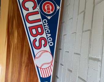 May include: A blue and red pennant with the words "CUBS" and "CHICAGO" in white lettering. The pennant features a baseball and a red circle with the word "CUBS" in white lettering. The pennant is made by WinCraft.