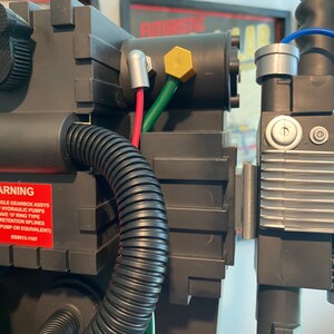 May include: A close-up of a black and silver Ghostbusters proton pack with a warning label that reads: "FOR-443 ANGLE GEARBOX ASSYS USE ONLY HYDRAULIC PUMPS THAT HAVE O-RING TYPE GREASE RETENTION SPLINES (87 WAF 200 PUMP OR EQUIVALENT) 550013-1167"