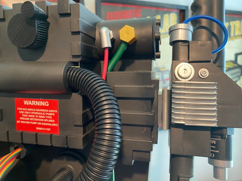 May include: A close-up of a black and silver Ghostbusters proton pack with a warning label that reads: "FOR-443 ANGLE GEARBOX ASSYS USE ONLY HYDRAULIC PUMPS THAT HAVE O-RING TYPE GREASE RETENTION SPLINES (87 WAF 200 PUMP OR EQUIVALENT) 550013-1167"