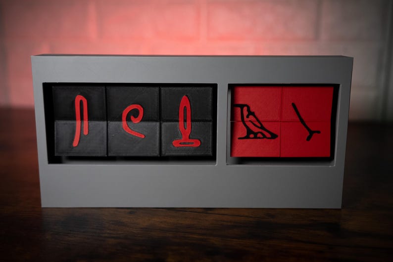 May include: A set of six black and red wooden blocks with hieroglyphic symbols carved into them. The blocks are arranged in a row in a gray frame.