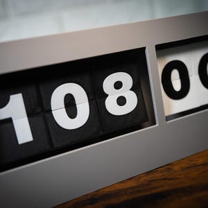 May include: A gray flip clock with black numbers displaying 10:08:00.