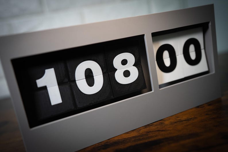 May include: A gray flip clock with black numbers displaying 10:08:00.