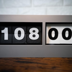 May include: A gray flip clock with black and white numbers displaying 10:08:00.
