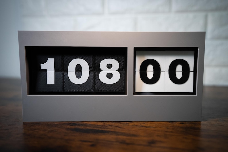 May include: A gray flip clock with black and white numbers displaying 10:08:00.