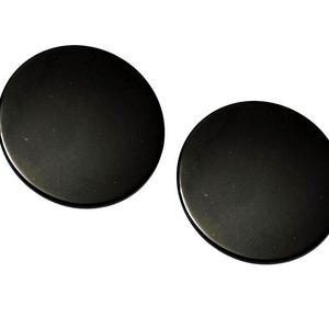 May include: Two solid black circular discs with smooth, flat surfaces. These round objects feature a uniform matte finish and a simple, clean design, presented as a pair of identical items against a plain white background.