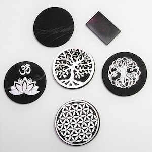 Könnte beinhalten: Sechs schwarze Untersetzer mit weißen Designs. Die Designs beinhalten einen Lebensbaum, eine Lotusblume mit dem Om-Symbol, eine Lebensblume und zwei verschiedene Baumdesigns.