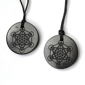 May include: Two black obsidian pendants with a black cord. Each pendant features a silver-colored geometric design, known as the Flower of Life.
