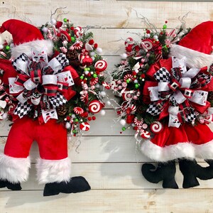 May include: Two Christmas wreaths featuring Santa Claus legs and a candy cane and bow theme. The wreaths are decorated with red, white, and green candy canes, bows, and other festive embellishments.