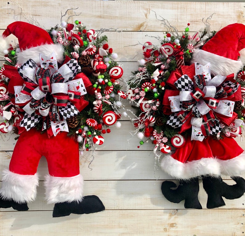 May include: Two Christmas wreaths featuring Santa Claus legs and a candy cane and bow theme. The wreaths are decorated with red, white, and green candy canes, bows, and other festive embellishments.