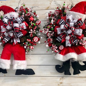 May include: Two Christmas wreaths with Santa and elf legs. The wreaths are decorated with red and white candy canes, red and white bows, and green and red berries.