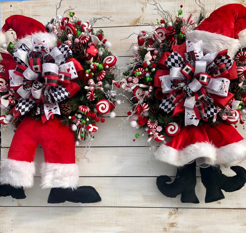 May include: Two Christmas wreaths with Santa and elf legs. The wreaths are decorated with red and white candy canes, red and white bows, and green and red berries.