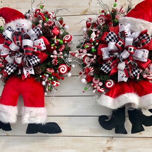 May include: Two Christmas wreaths with Santa Claus legs and hats. The wreaths are decorated with red and white candy canes, green and red berries, and a black and white checkered bow.