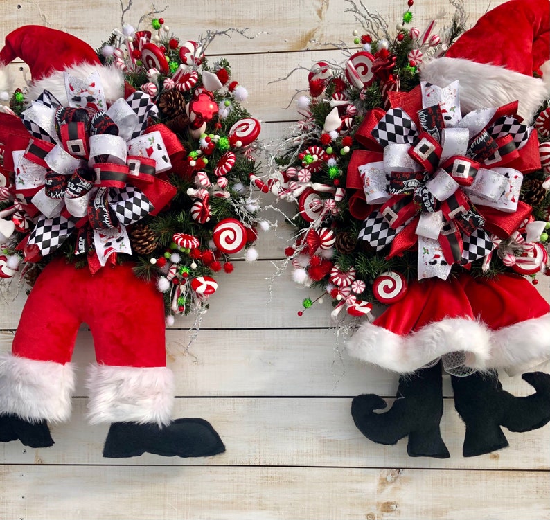 May include: Two Christmas wreaths with Santa Claus legs and hats. The wreaths are decorated with red and white candy canes, green and red berries, and a black and white checkered bow.