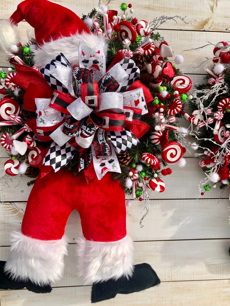 May include: A red and white Christmas wreath with a Santa Claus figure, a large black and white bow, and candy cane decorations.