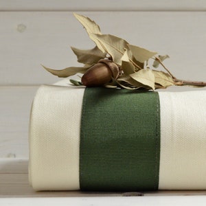 Peut inclure: Un rouleau de tissu blanc avec un ruban vert. Le tissu a une texture subtile. Le ruban est large et a une texture côtelée subtile.
