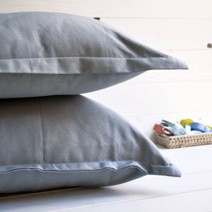 Può includere: Due federe di colore azzurro chiaro con una texture sottile e un bordo bianco. Le federe sono impilate l'una sull'altra.