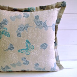 May include: A beige pillow with a floral pattern and blue butterflies. The pillow has a light brown border.