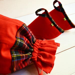 Könnte beinhalten: Zwei rote Stoffgeschenktüten mit kariertem Besatz und Kordelzug. Die Taschen sind aus weichem, rotem Stoff mit einem karierten Besatz am oberen Rand. Die Taschen haben einen Kordelzug und sind perfekt für kleine Geschenke.