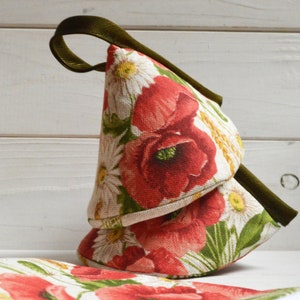 Peut inclure: Deux maniques de cuisine en forme de cône, avec un motif floral rouge, blanc et vert. Les maniques ont une anse en tissu vert.