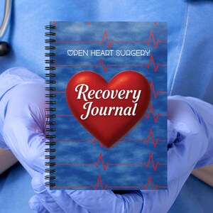 May include: A spiral-bound journal with a blue background featuring red EKG heart rhythm lines. The cover displays the text "OPEN HEART SURGERY" in white and "Recovery Journal" in a large, bold white script font centered over a red heart.