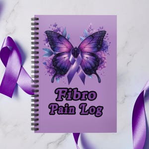 May include: A spiral-bound notebook with a light purple cover featuring a dark purple butterfly with a central awareness ribbon and floral accents. The text "Fibro Pain Log" is printed in bold black letters below the butterfly graphic.