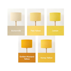 May include: Five cylindrical lamp shades in varying shades of yellow, labelled Buttermilk, Pale Yellow, Lemon, Golden Mustard Yellow, and Honey Yellow. Each shade is mounted on a simple wooden stand, showcasing a range of warm, sunny tones.