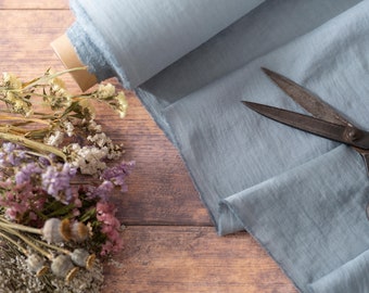 May include: A roll of light blue fabric with a pair of vintage scissors on top. Dried flowers are in the lower left corner of the image.