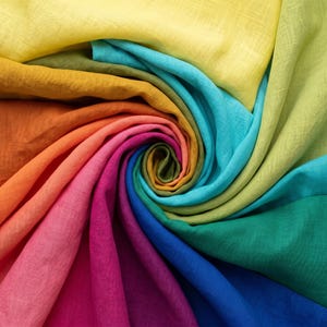 May include: A close-up of a spiral arrangement of colourful fabric. The fabric displays a rainbow of hues, including yellow, orange, pink, purple, blue, green, and teal. The material appears to be light and flowing, creating a visually striking pattern.