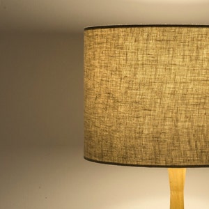 May include: A beige lampshade with a textured fabric finish. The lampshade is attached to a wooden base.