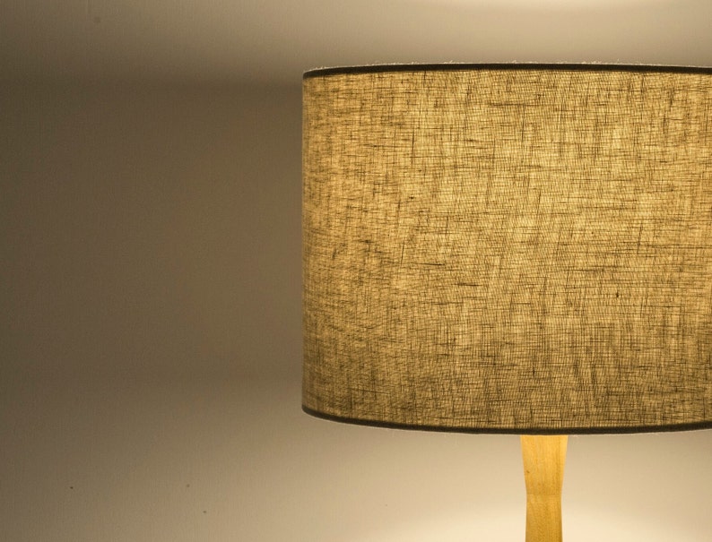 May include: A beige lampshade with a textured fabric finish. The lampshade is attached to a wooden base.