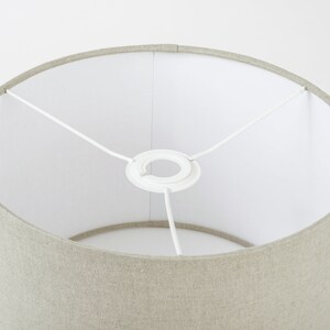 May include: A beige linen lampshade with a white fabric lining and a white metal ring at the top.