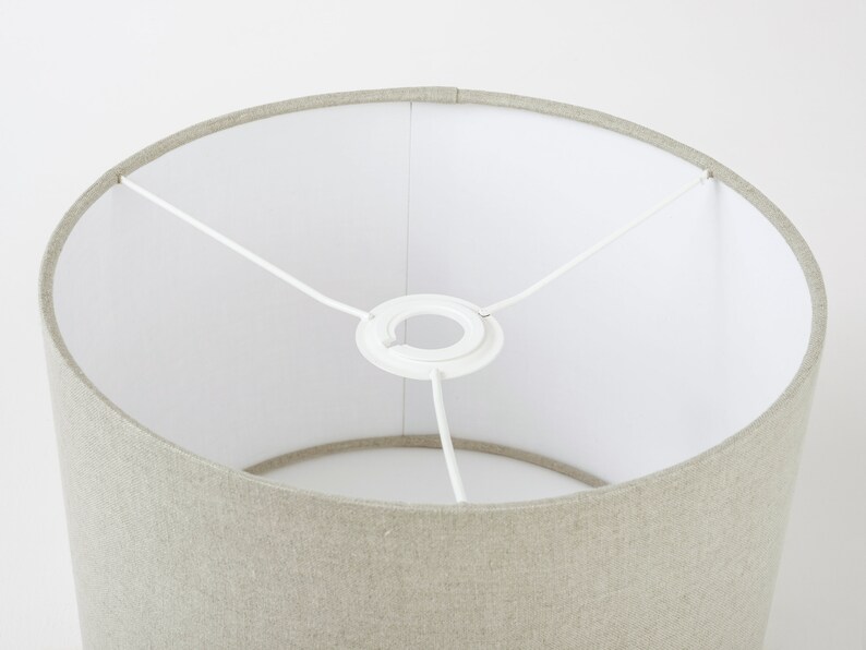 May include: A beige linen lampshade with a white fabric lining and a white metal ring at the top.
