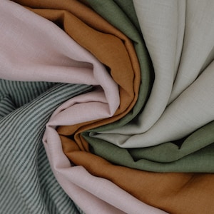 Puede incluir: Una colecci&oacute;n de muestras de tela dispuestas en espiral, con colores s&oacute;lidos en rosa claro, ocre c&aacute;lido, verde oliva y blanco roto, junto a una secci&oacute;n de tela con un patr&oacute;n de rayas finas en verde oscuro y blanco.