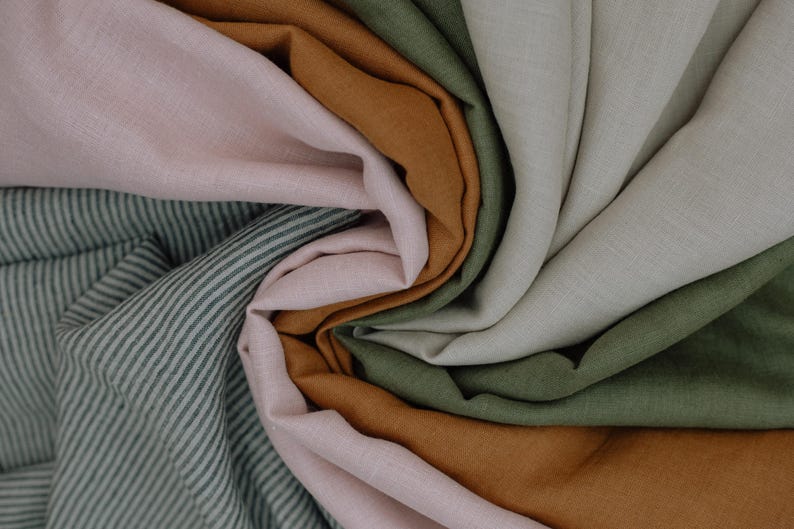 Puede incluir: Una colecci&oacute;n de muestras de tela dispuestas en espiral, con colores s&oacute;lidos en rosa claro, ocre c&aacute;lido, verde oliva y blanco roto, junto a una secci&oacute;n de tela con un patr&oacute;n de rayas finas en verde oscuro y blanco.