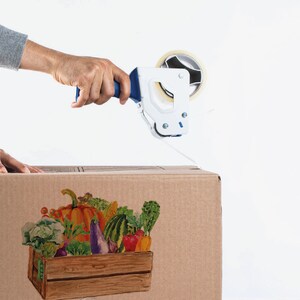 May include: A person is sealing a cardboard box with tape. The box has a colorful illustration of a wooden crate filled with fresh produce, including a pumpkin, eggplant, and various vegetables.
